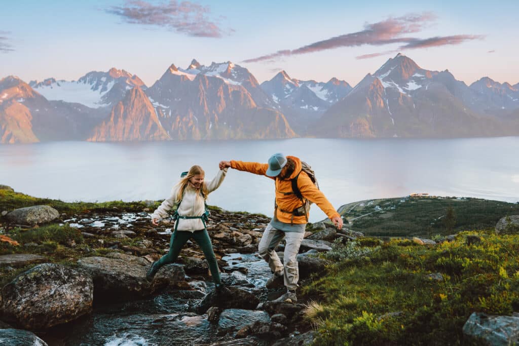 Couple hiking in Norway man helps woman cross river in mountains healthy lifestyle outdoor active family vacations adventure tour, friends exploring Lyngen Alps